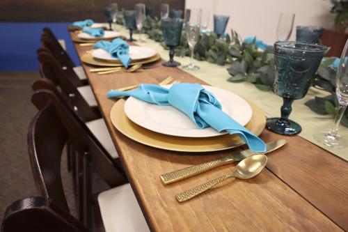 Farm table with brown garden chairs, gold flatware, blue goblets and turquoise napkins